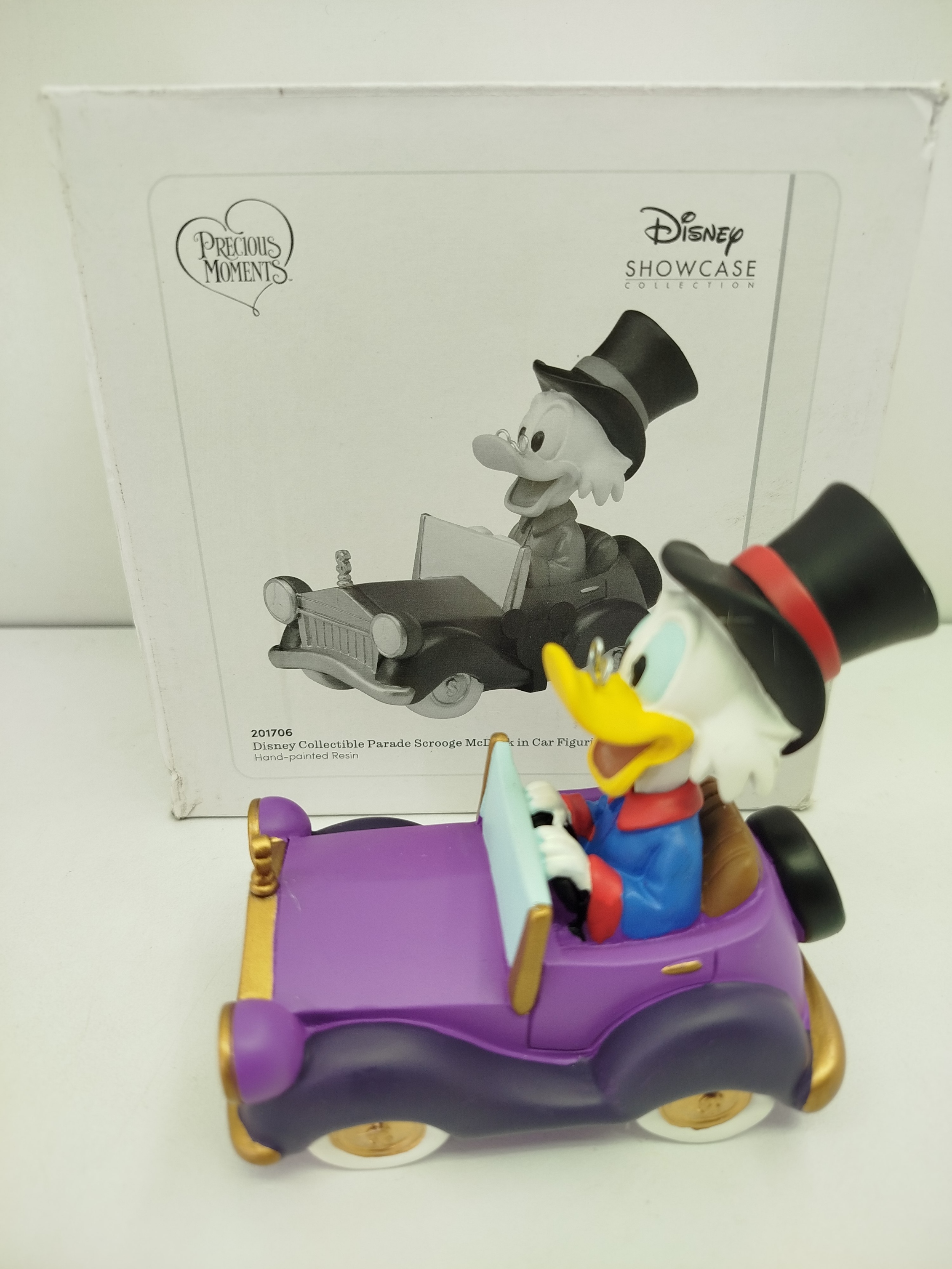 Disney Collectible Parade Scrooge McDuck de Precious Moments, en la que el Tio Rico (Scrooge McDuck) conduce un elegante auto de color morado con sombrero de copa