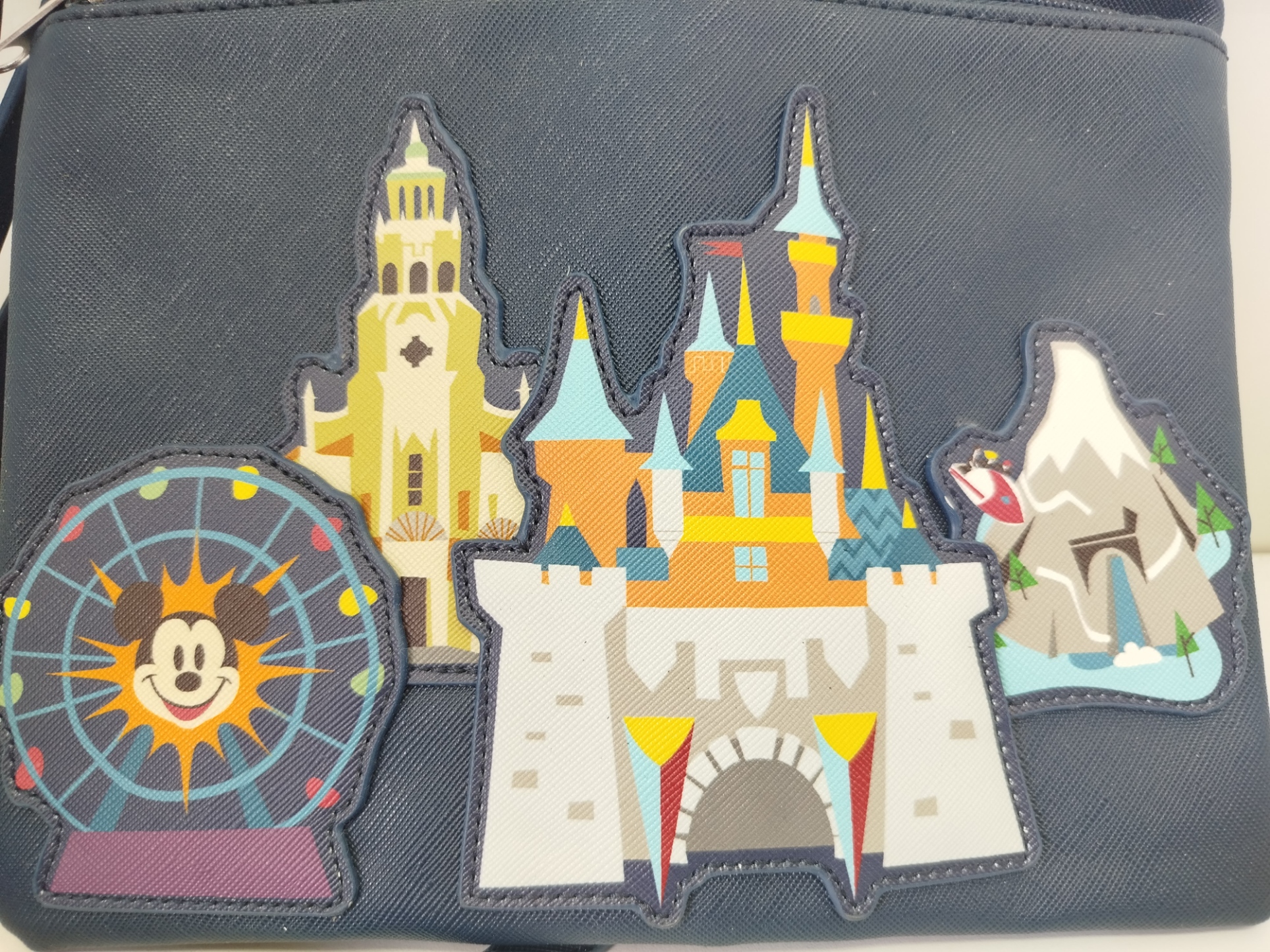 Bolso azul marino de Disneyland con  parches acolchados de atracciones icónicas como el castillo y la rueda de la fortuna en el frente