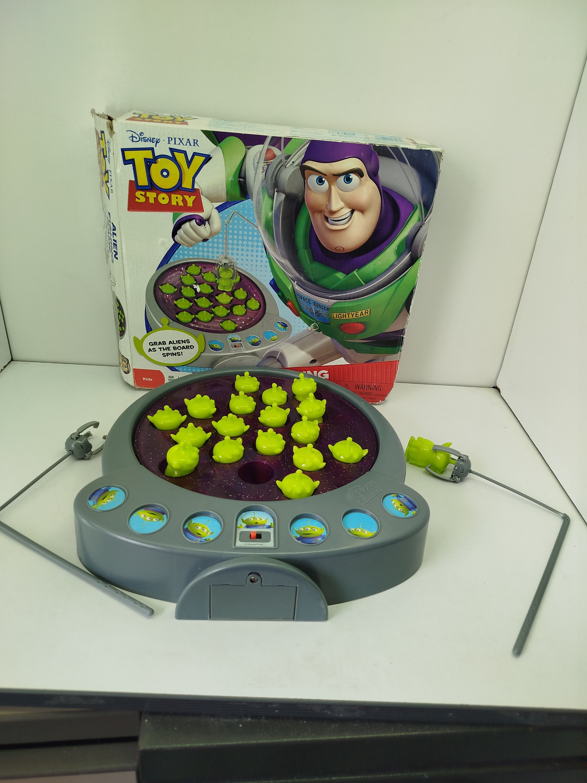  Toy Story 3 Alien Fishing Game-  juego de pesca motorizado, se utiliza cañas con "garras" para atrapar a  marcianitos verdes de Pizza Planet mientras el tablero gira.